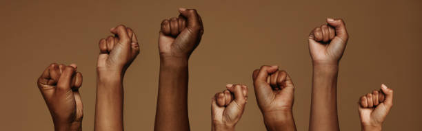 Seven Black Fist across all shades of skin tone raising their fist in the air.